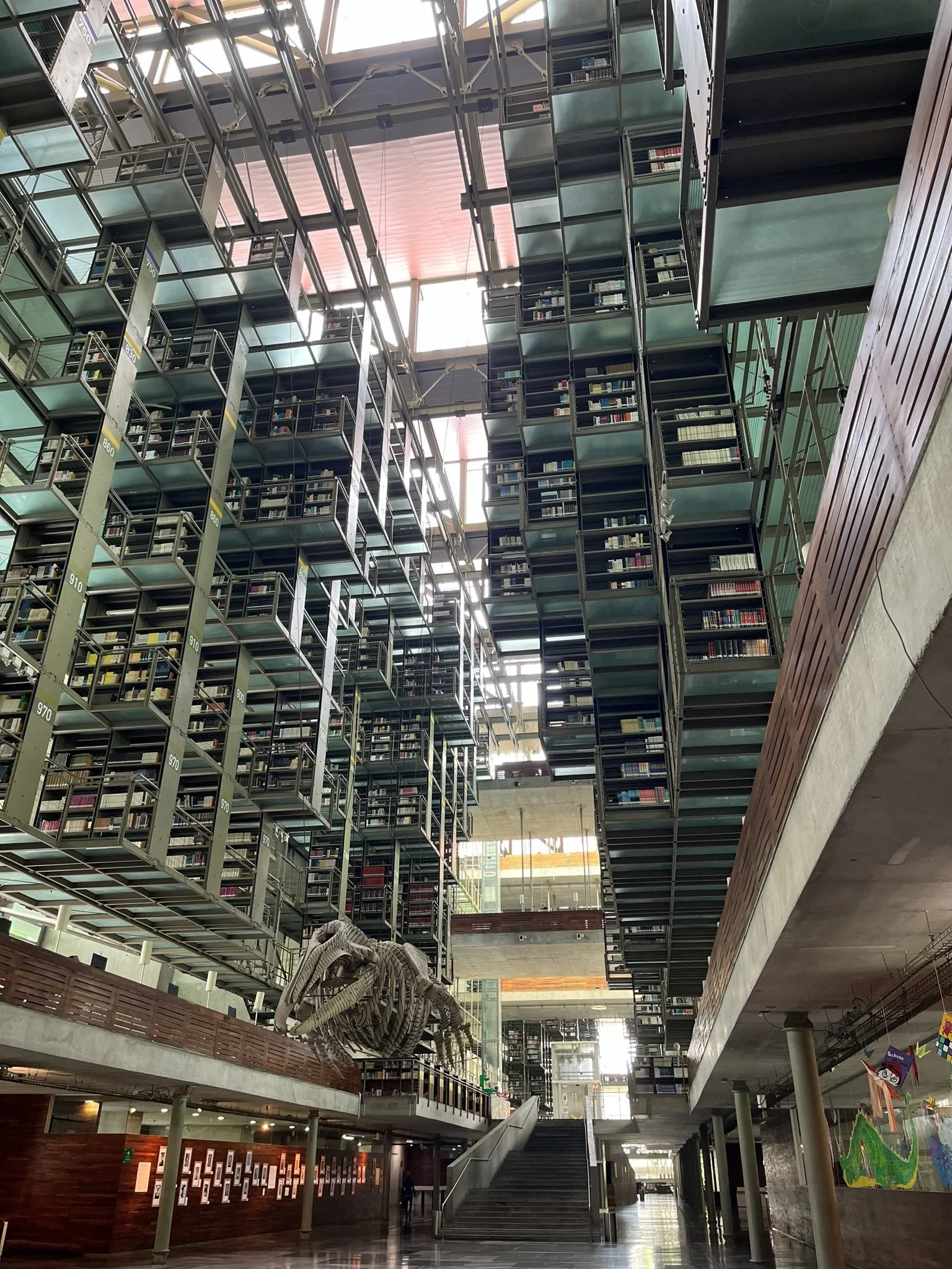 Interior view of the Biblioteca Vasconcelos in Mexico City with multiple floors, open space, bookshelves, and a dinosaur skeleton exhibit.
