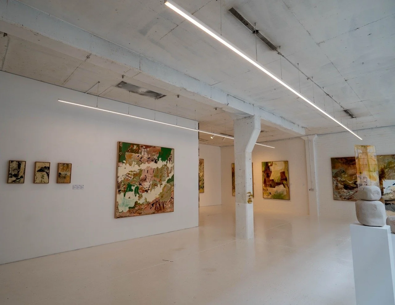 A modern art gallery with abstract paintings on white walls, bright lighting, and a white pillar in the center.