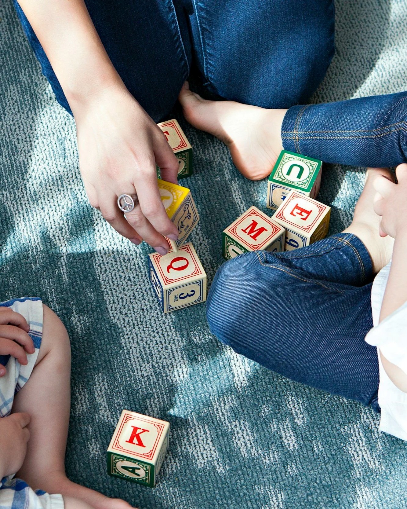 Children sitting on a carpeted floor playing with colorful alphabet and number blocks.