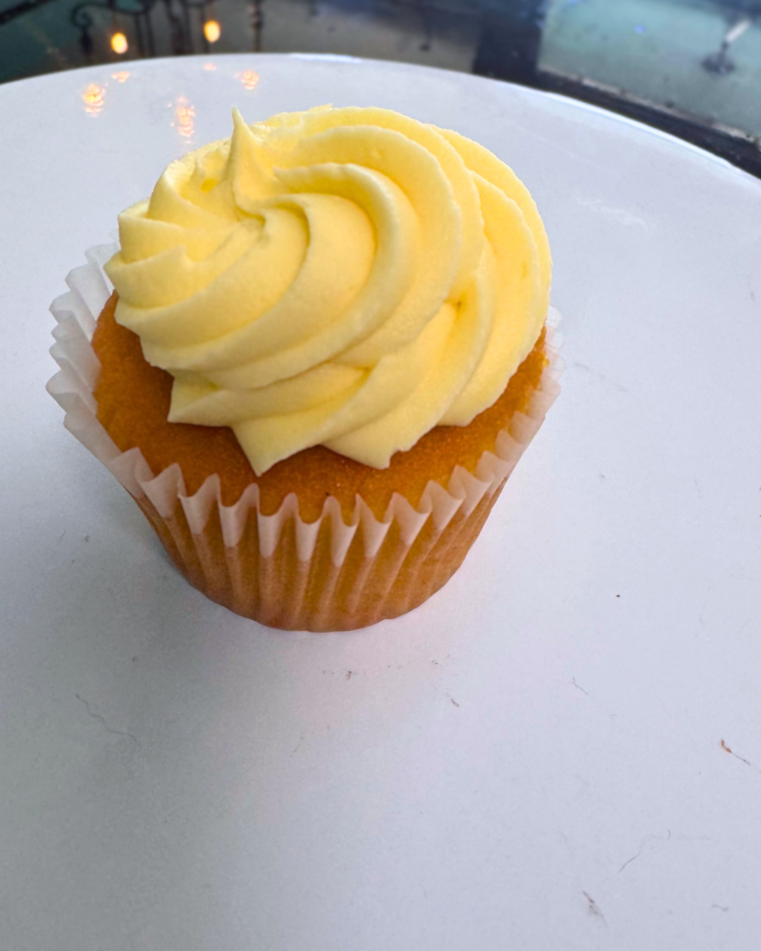 Cupcake with yellow frosting on a white surface near a window