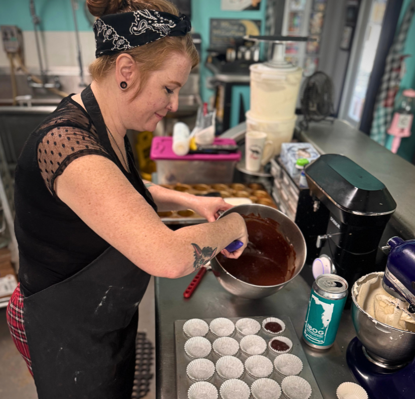 Woman pouring chocolate into cupcake liners in a bakery kitchen.