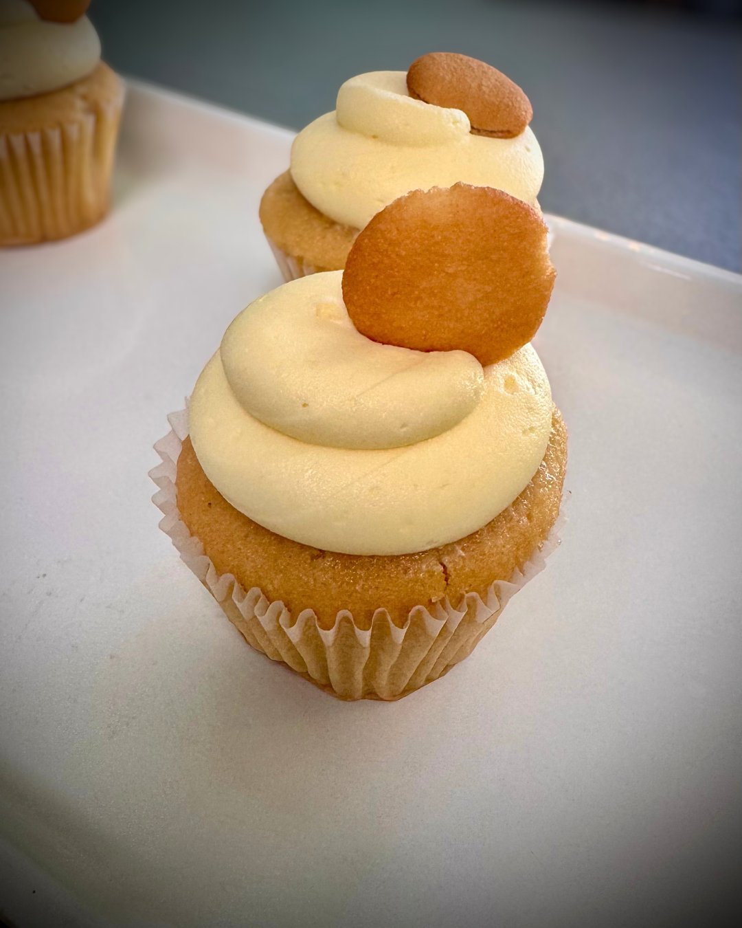 Cupcake with vanilla frosting topped with a round cookie on a white surface.