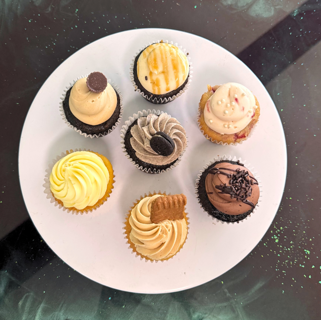A white plate with nine assorted cupcakes, each decorated with various frosting and toppings, arranged in a circular pattern.