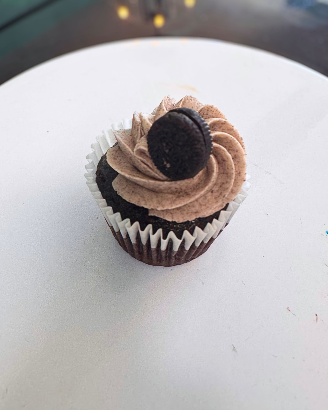 Chocolate cupcake with chocolate frosting and an Oreo cookie on top, in a white cupcake liner, on a white surface.