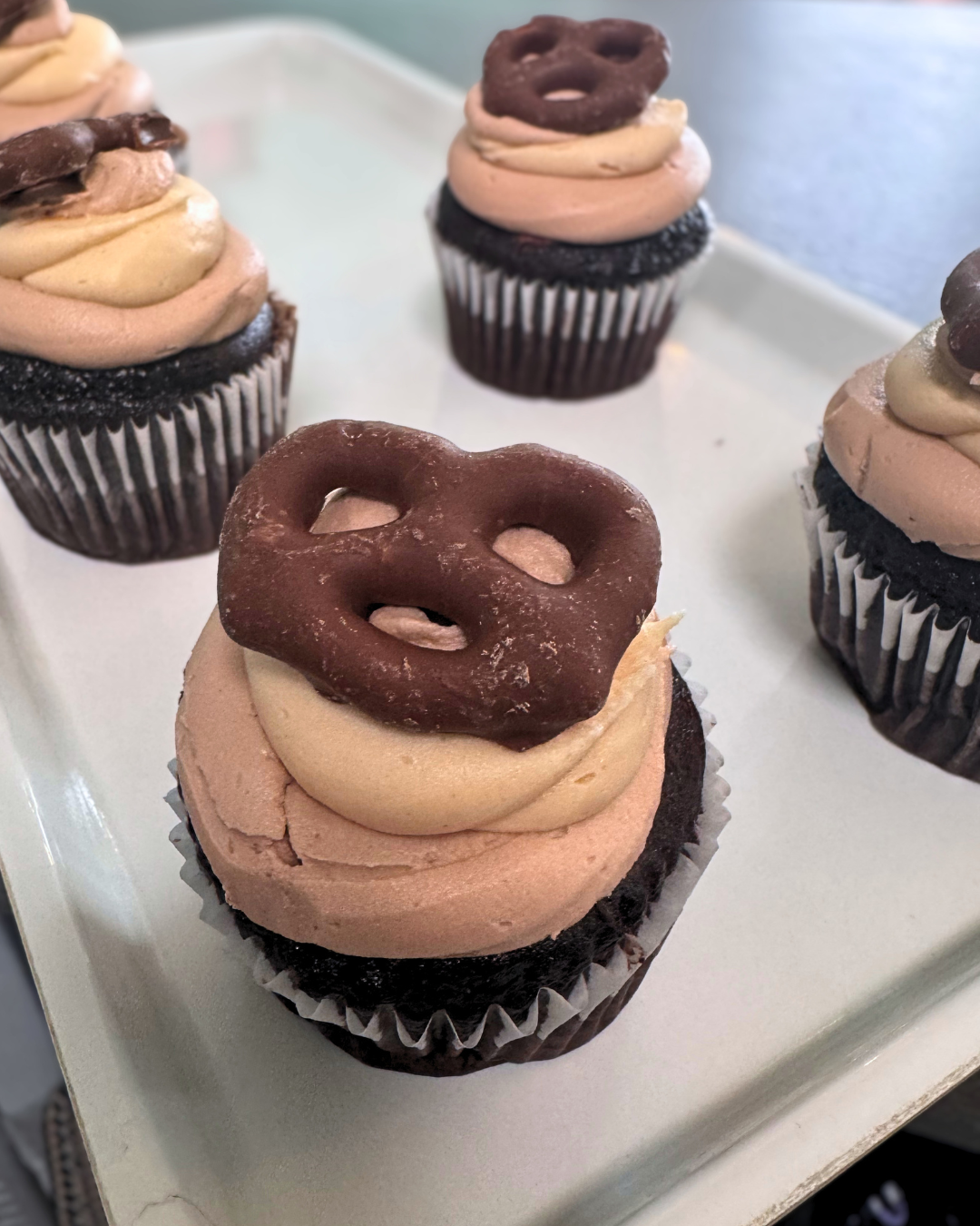 Chocolate cupcakes topped with swirled chocolate and vanilla frosting, decorated with edible pretzels on top.