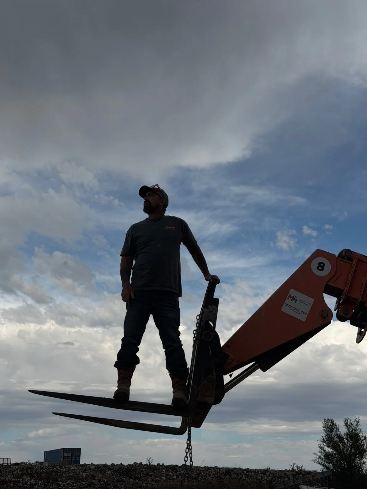 A man standing on a construction machine platform with a cloudy sky in the background.