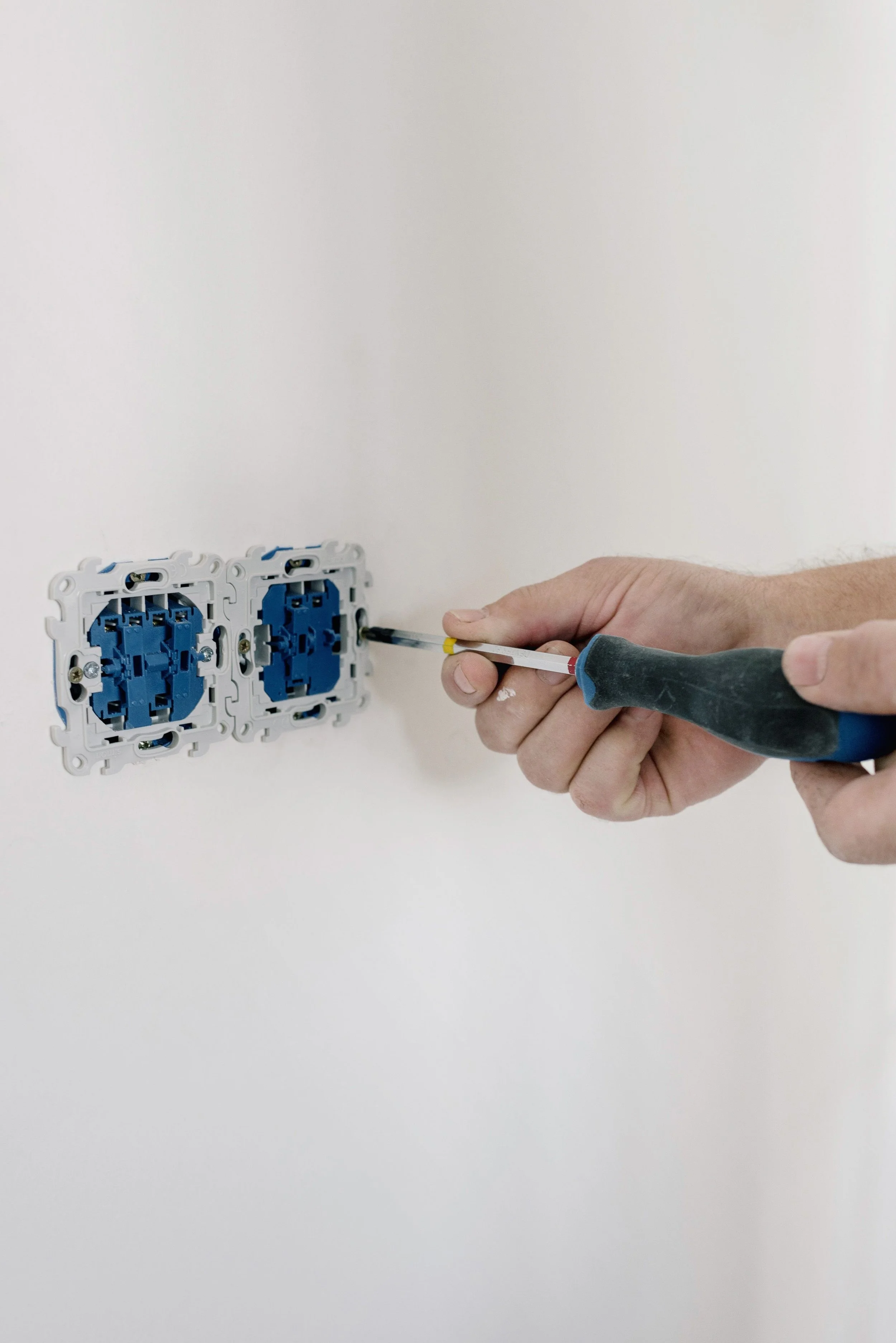 Person installing a light switch on a white wall using a screwdriver.
