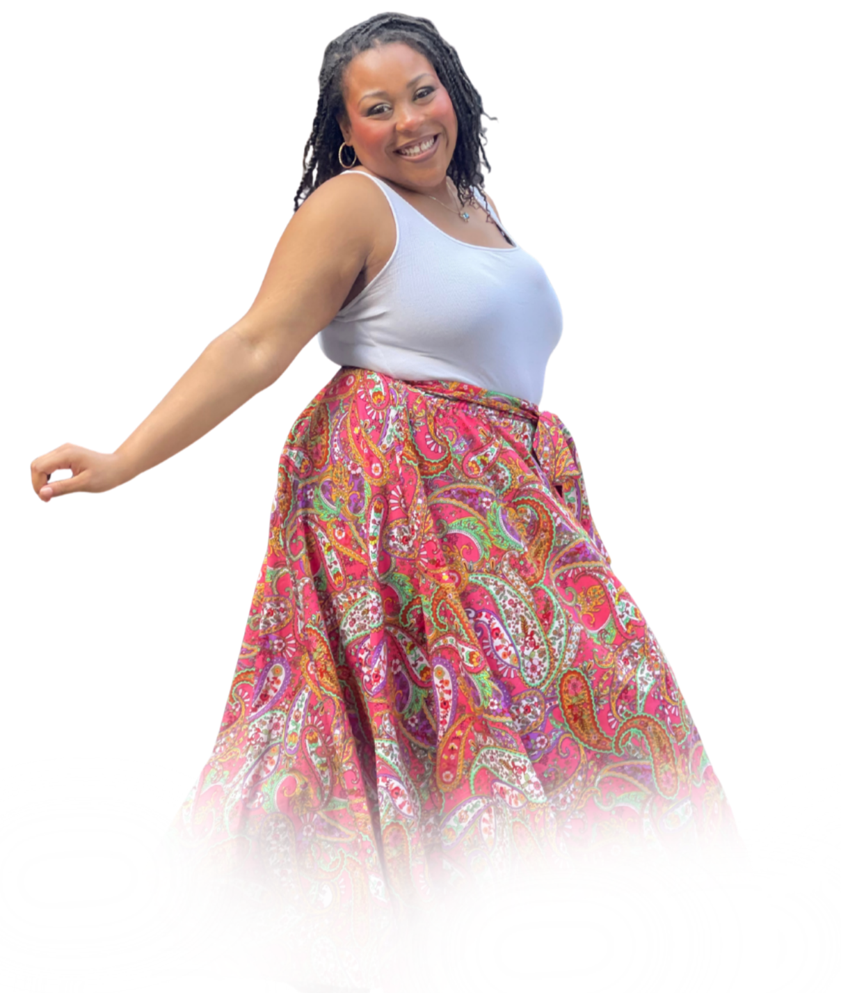 A smiling woman with dreadlocks wearing a white sleeveless top and a colorful paisley long skirt.