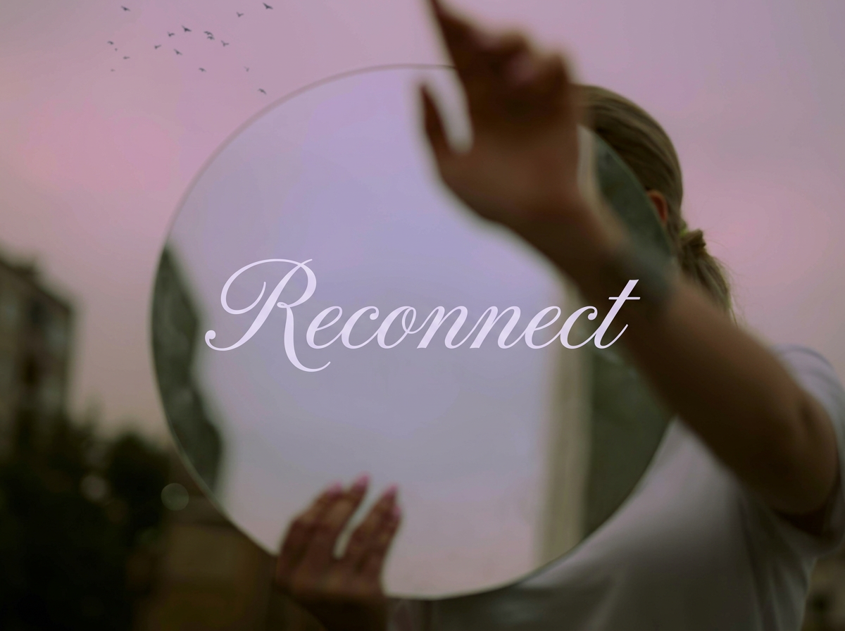 A person holds a mirror at an angle reflecting the sky and birds flying in the background. The word 'Reconnect' is overlaid on the mirror.
