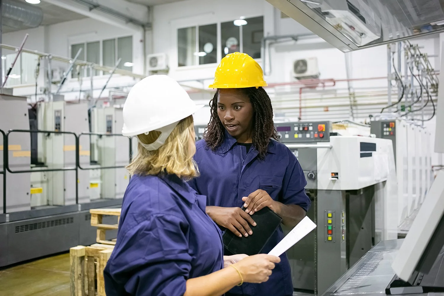 Think-Resilience-diverse-female-factory-employees-hardhats-overalls-standing-plant-floor-chatting.jpg