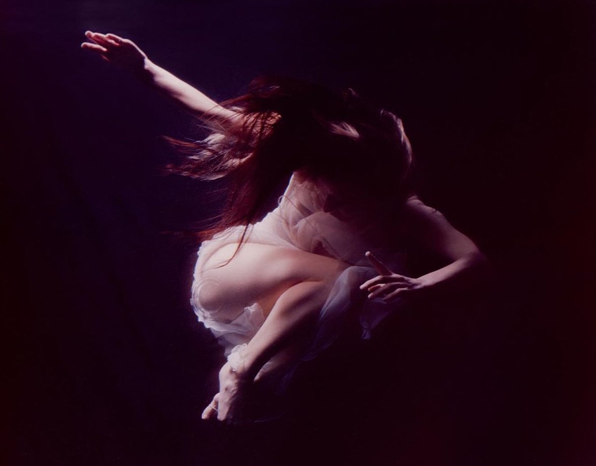 Two people dancing intimately on a dark stage with dramatic lighting.