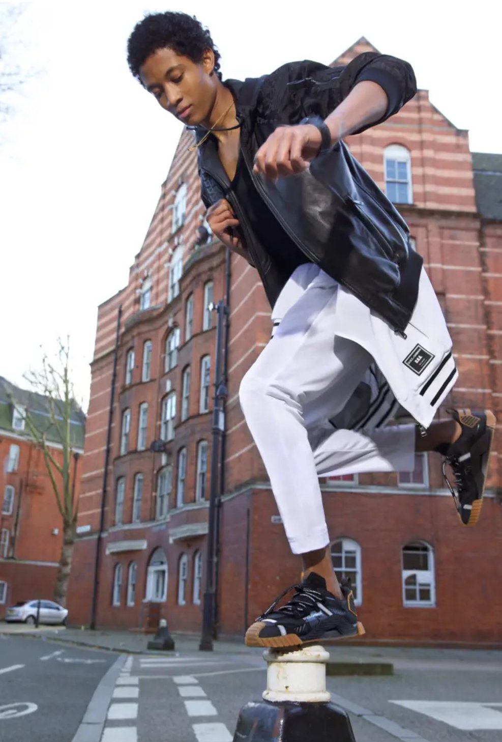 A young man balancing on a pole in an urban setting with red brick buildings in the background.