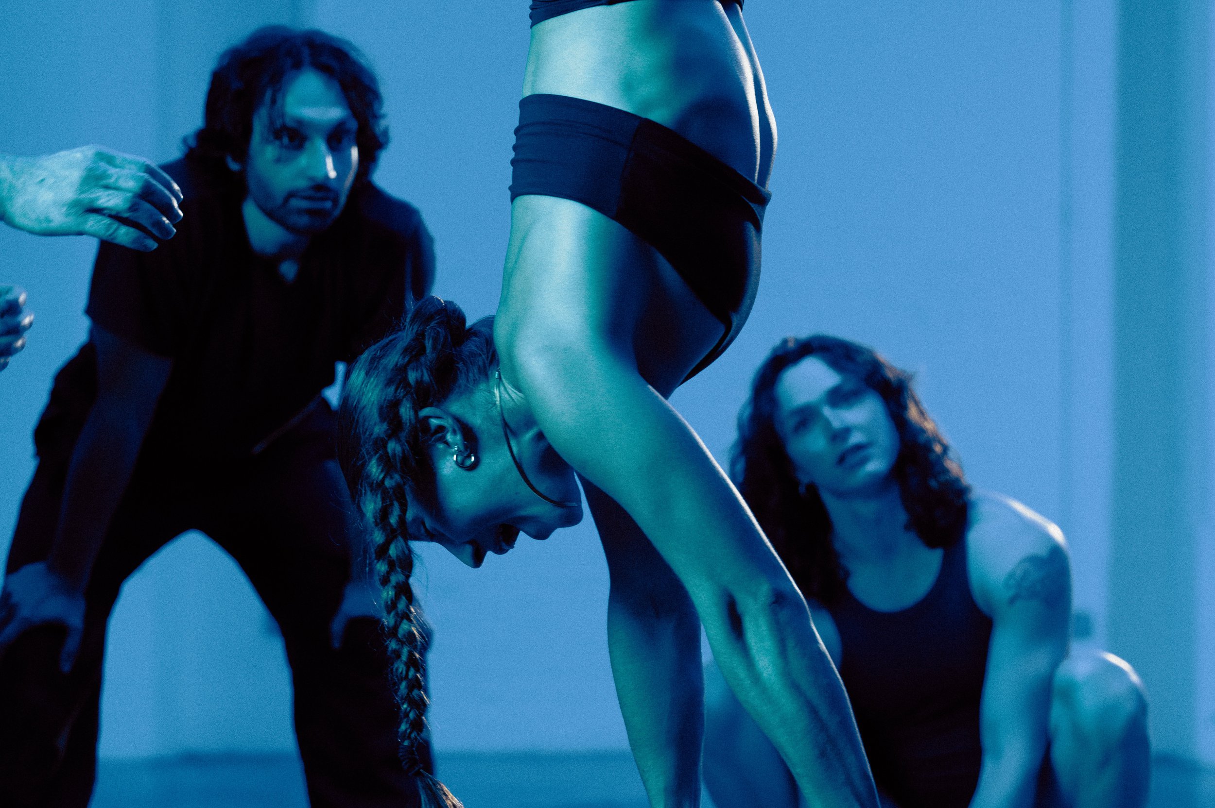 A group of women in athletic wear are participating in a fitness class or yoga session, with a blue lighting ambiance.
