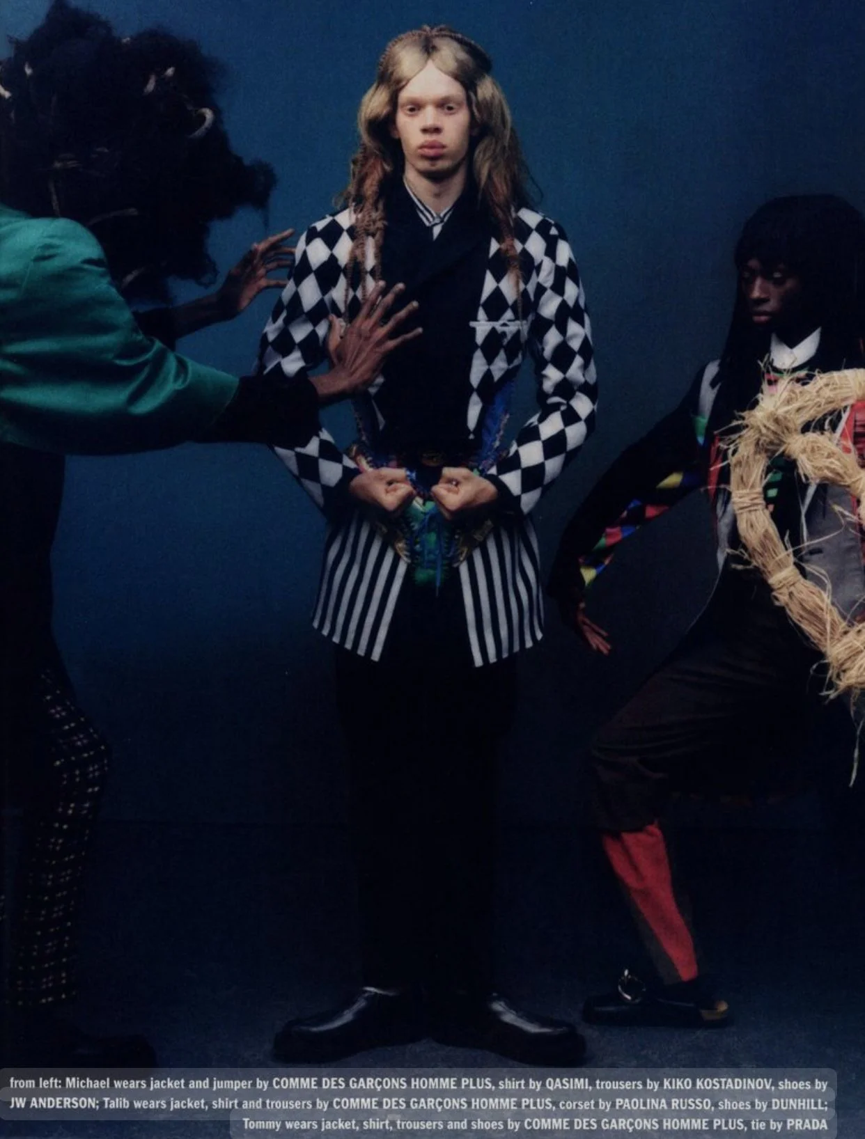 Fashion photoshoot with three models in colorful, patterned clothing and accessories against a dark blue background.