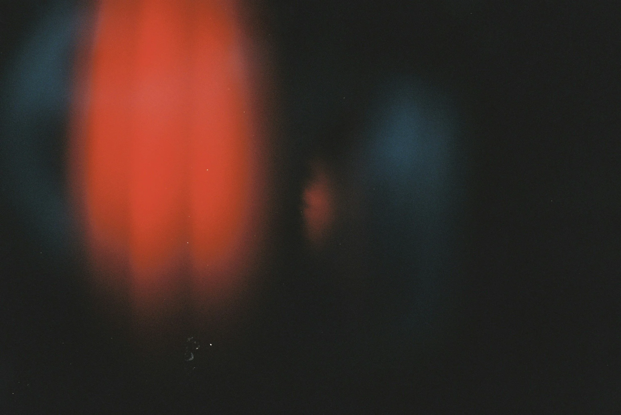 A dark image with blurred red and blue lights and some small white specks.