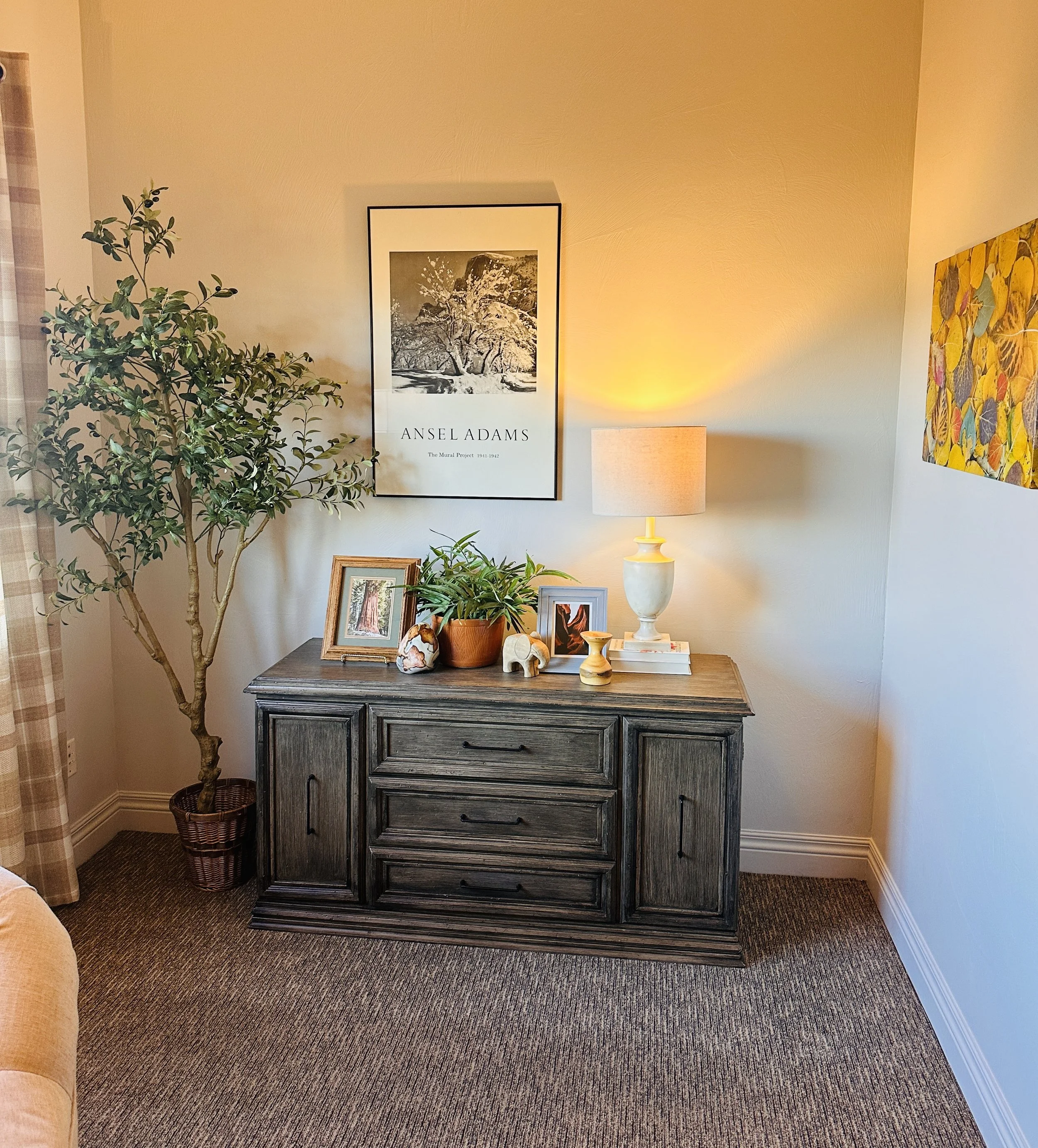 Dark dresser with black and white framed art print and potted tree, table lamp