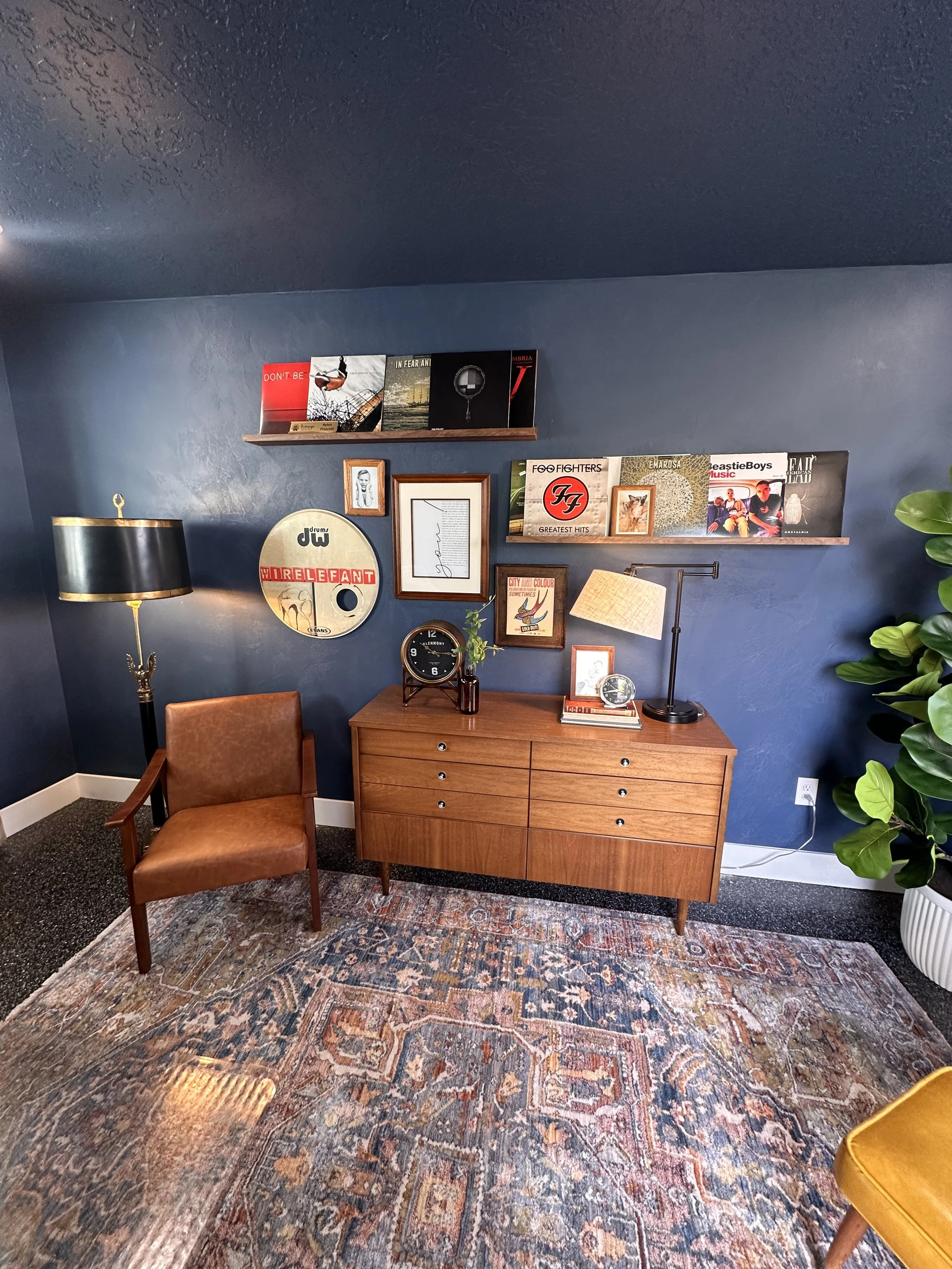 Navy accent nook with wood dresser, leather chair, mustard ottoman, and gallery wall