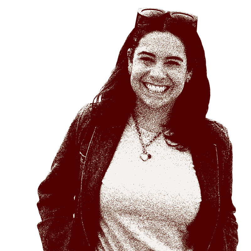 A woman smiling, wearing sunglasses on her head, a necklace, a light-colored shirt, and a dark jacket against a black background.