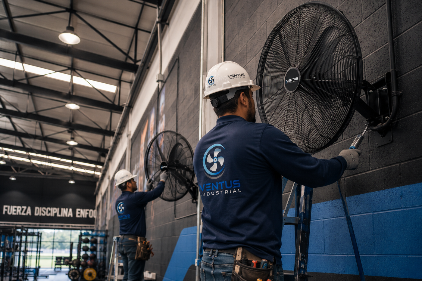 Dos empleados de Ventus Industrial limpiando ventiladores grandes en una pared de un gimnasio o área de entrenamiento.