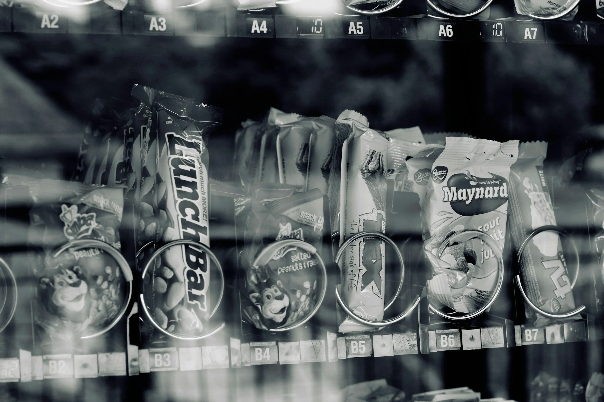 Vending machine with snack packets inside, including chips and fruit snacks, behind a glass panel labeled with row and column identifiers.