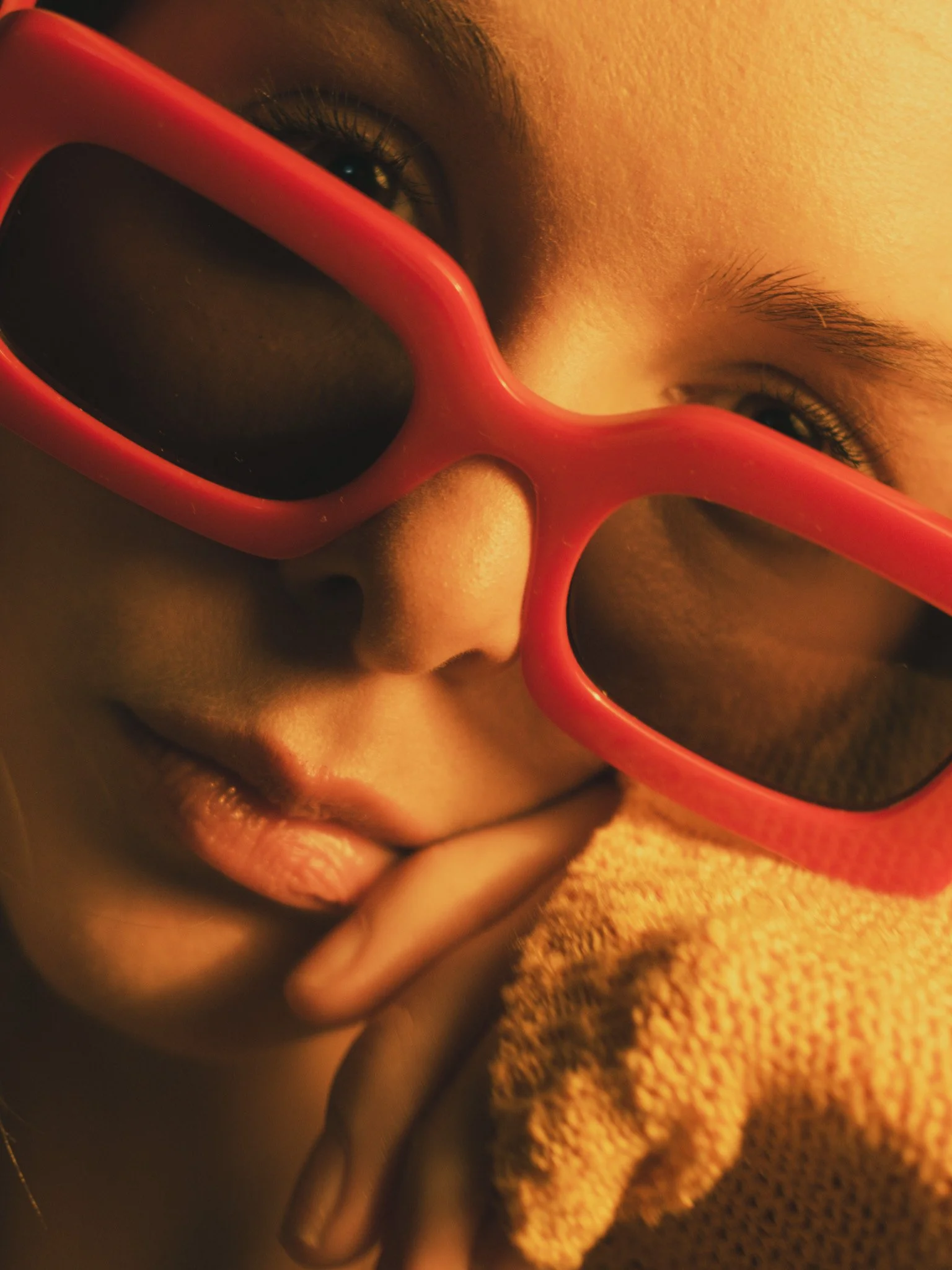 Close-up of a person's face with glasses, lying on a textured blanket or towel. The person's eyes and nose are visible, and the glasses have a bright red frame.