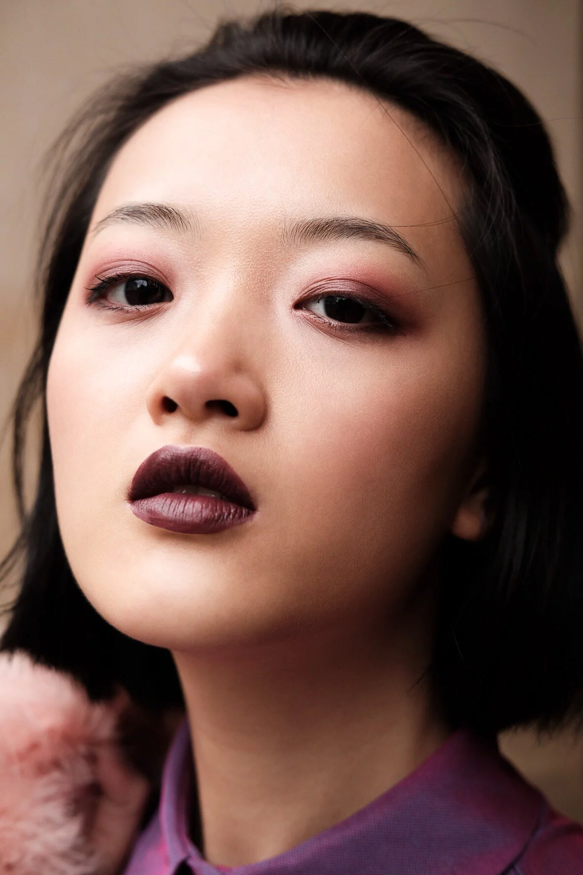 A close-up of a woman with dark hair, eye makeup, and dark lipstick, looking slightly to the side.