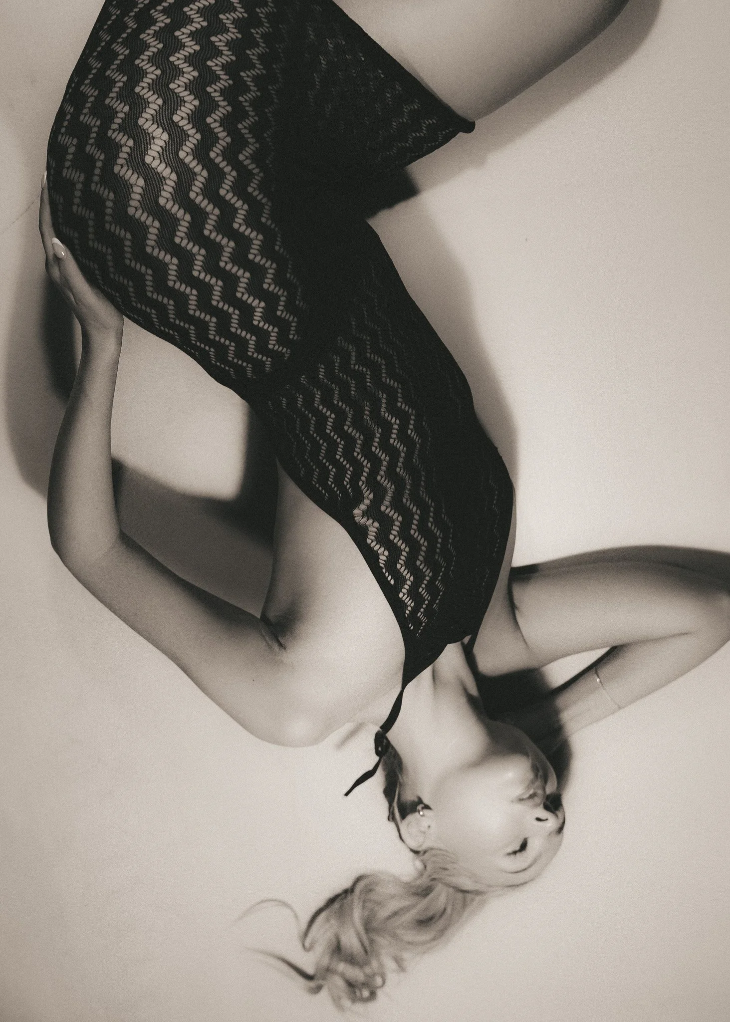 Black and white photo of a woman lying on a white surface, wearing lace leggings and high heels, with platinum blonde hair flowing around her.
