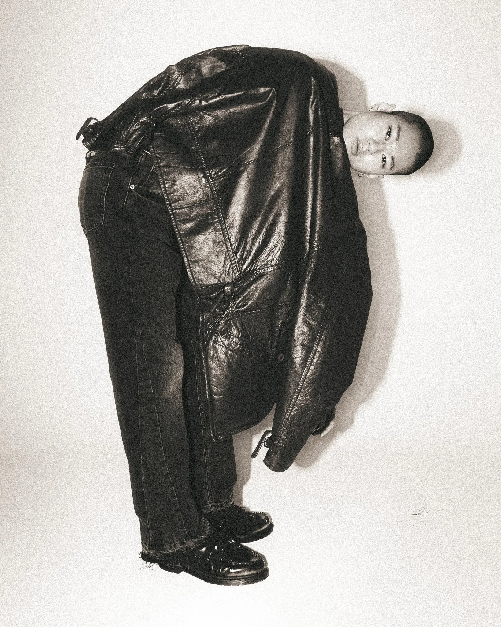A person wearing black leather pants, a black leather jacket, and black boots, standing against a plain white background.