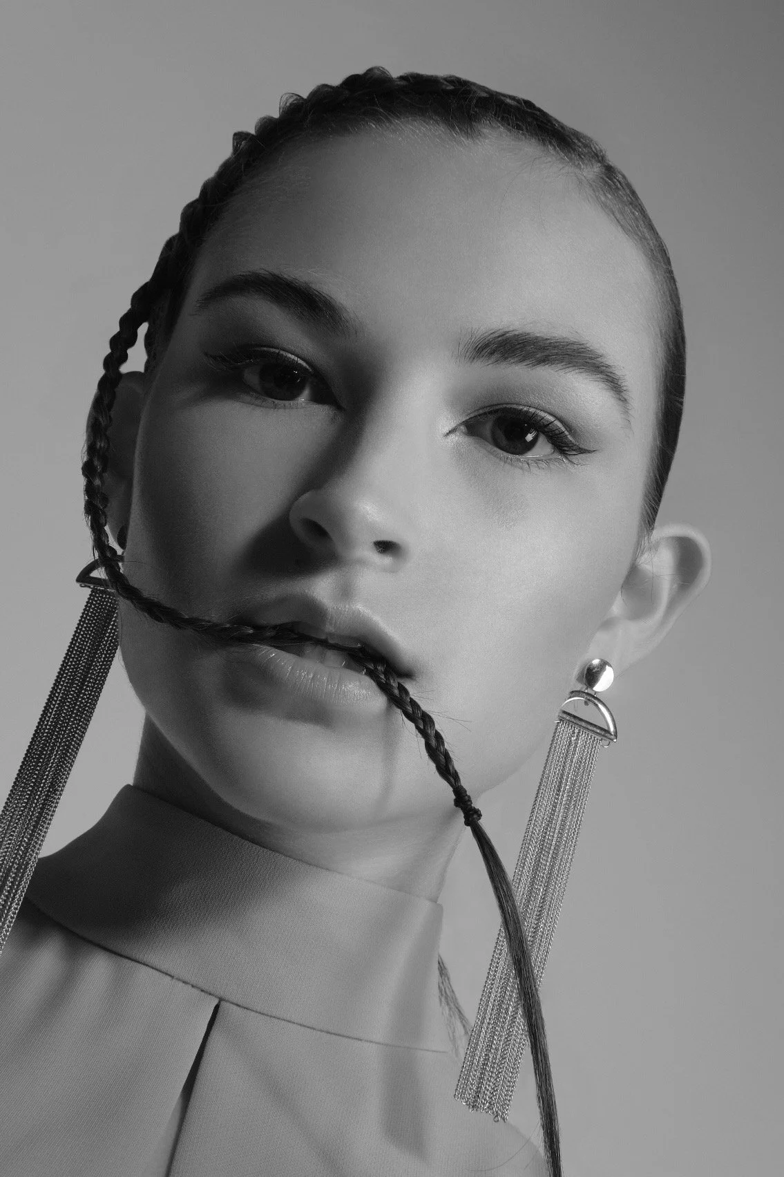 Black and white portrait of a woman with braided hair, wearing large earrings with chains and a collared top.