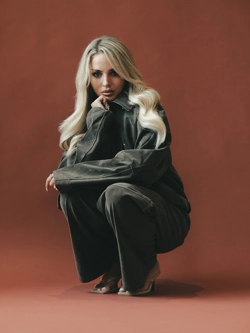 AVA × CAMR — fashion portrait in oversized dark denim against a warm red studio backdrop, photographed by CAMR Visuals.
