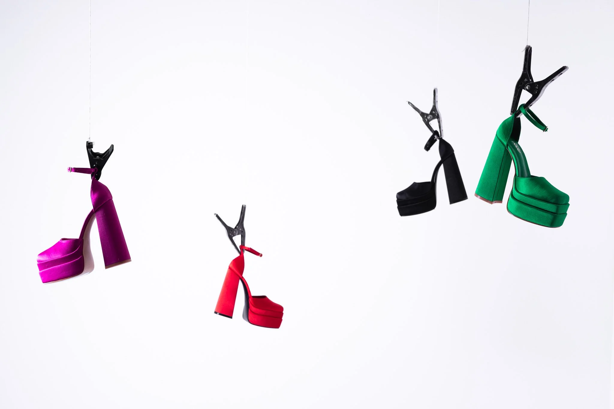 Colorful high-heeled shoes hanging on a wire against a white background.