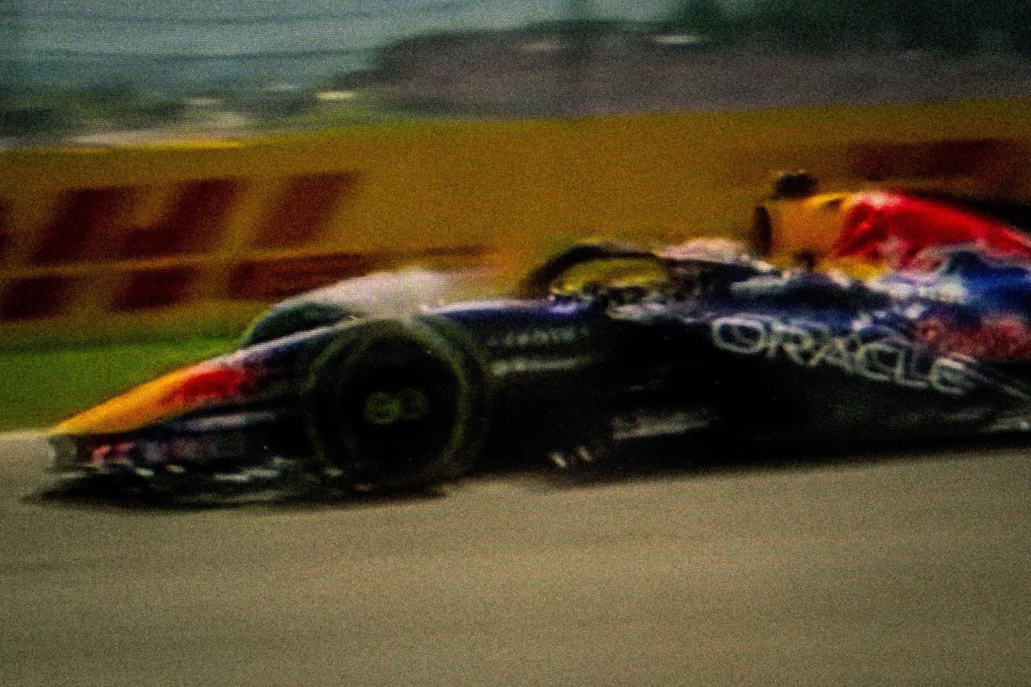 A race car speeds on a track, with a yellow vehicle visible in the background and debris on the ground.