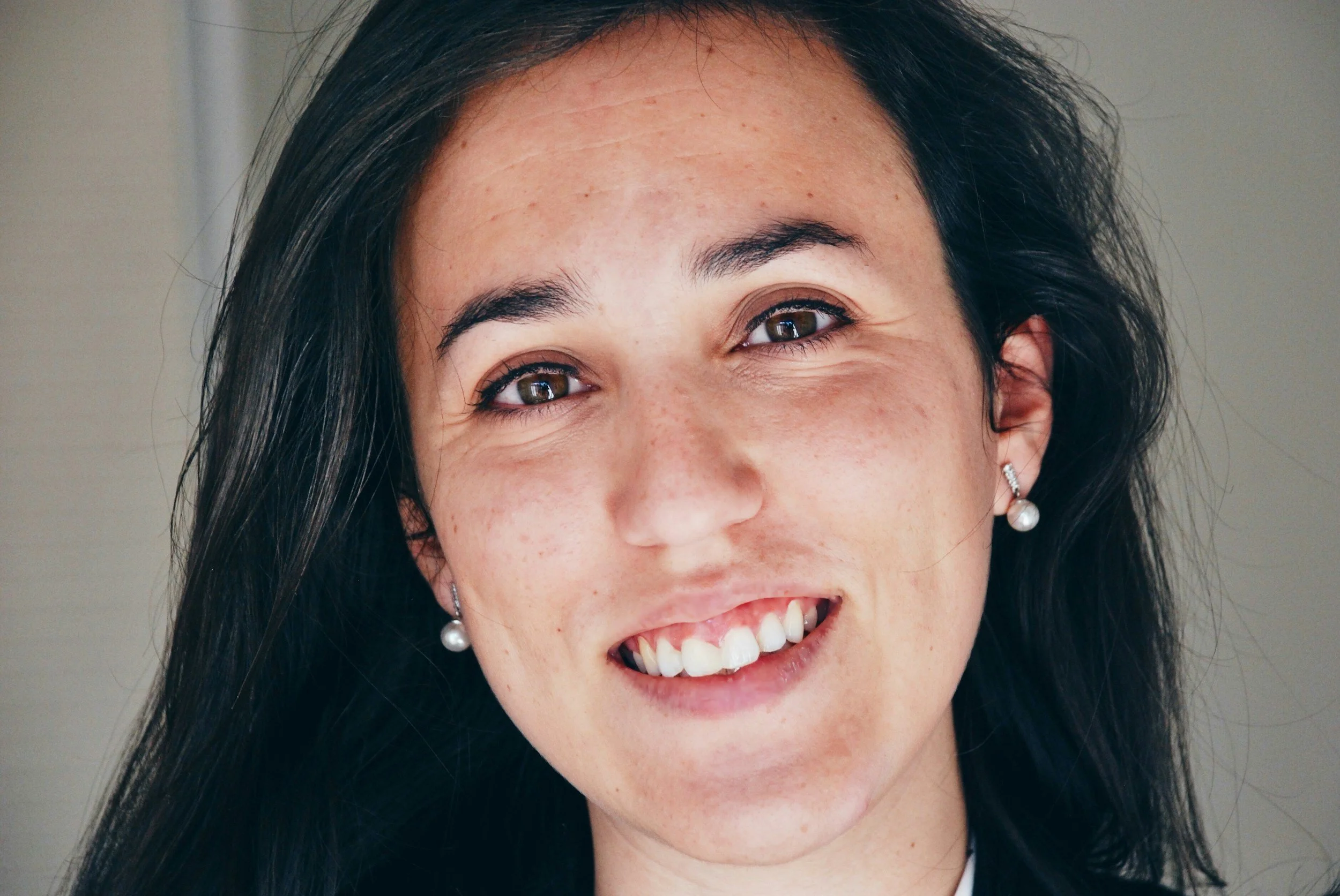 Smiling woman with dark hair, brown eyes, and pearl earrings.