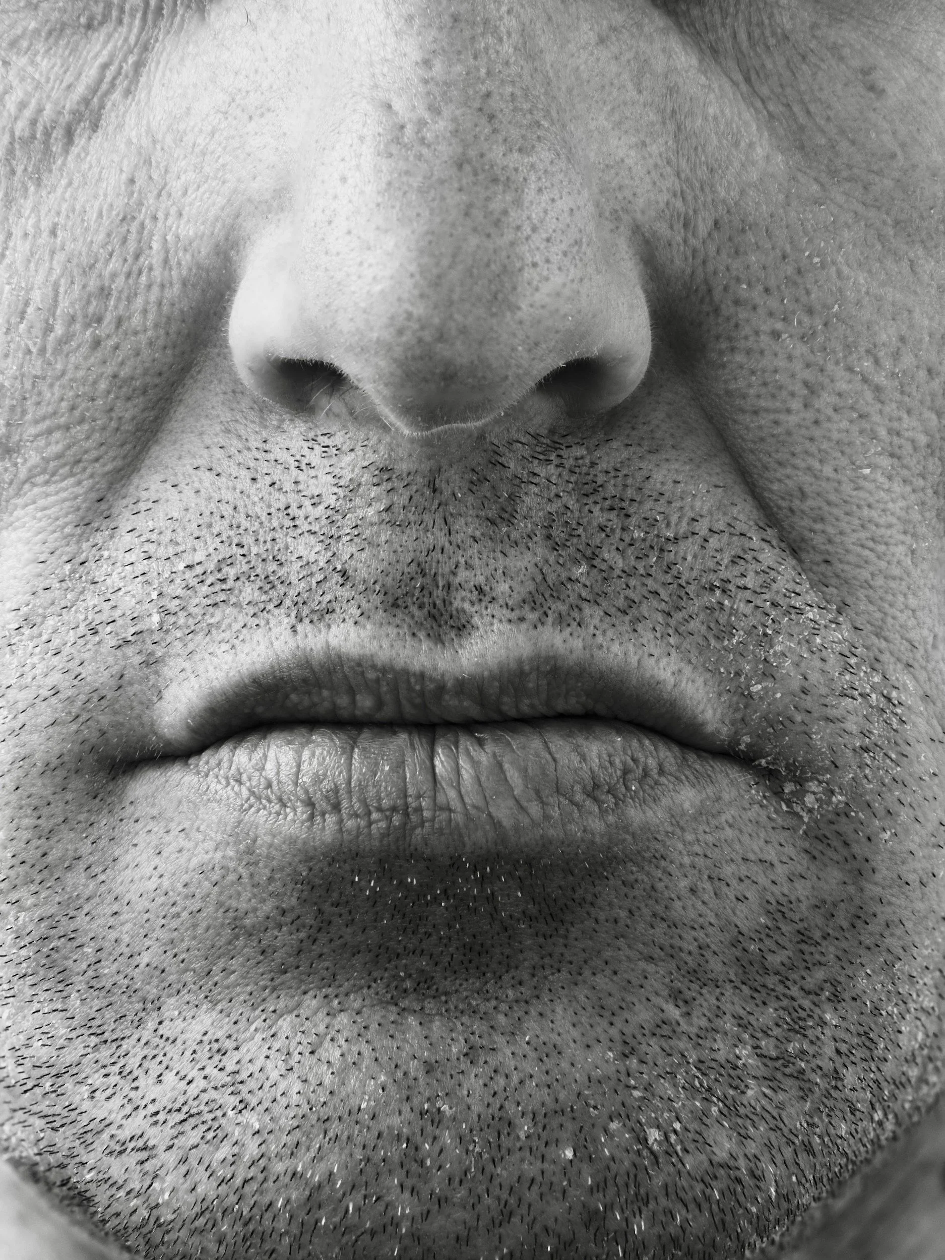 Close-up black and white photograph of a person's nose and mouth with visible facial hair and pores and deep set nasolabial folds