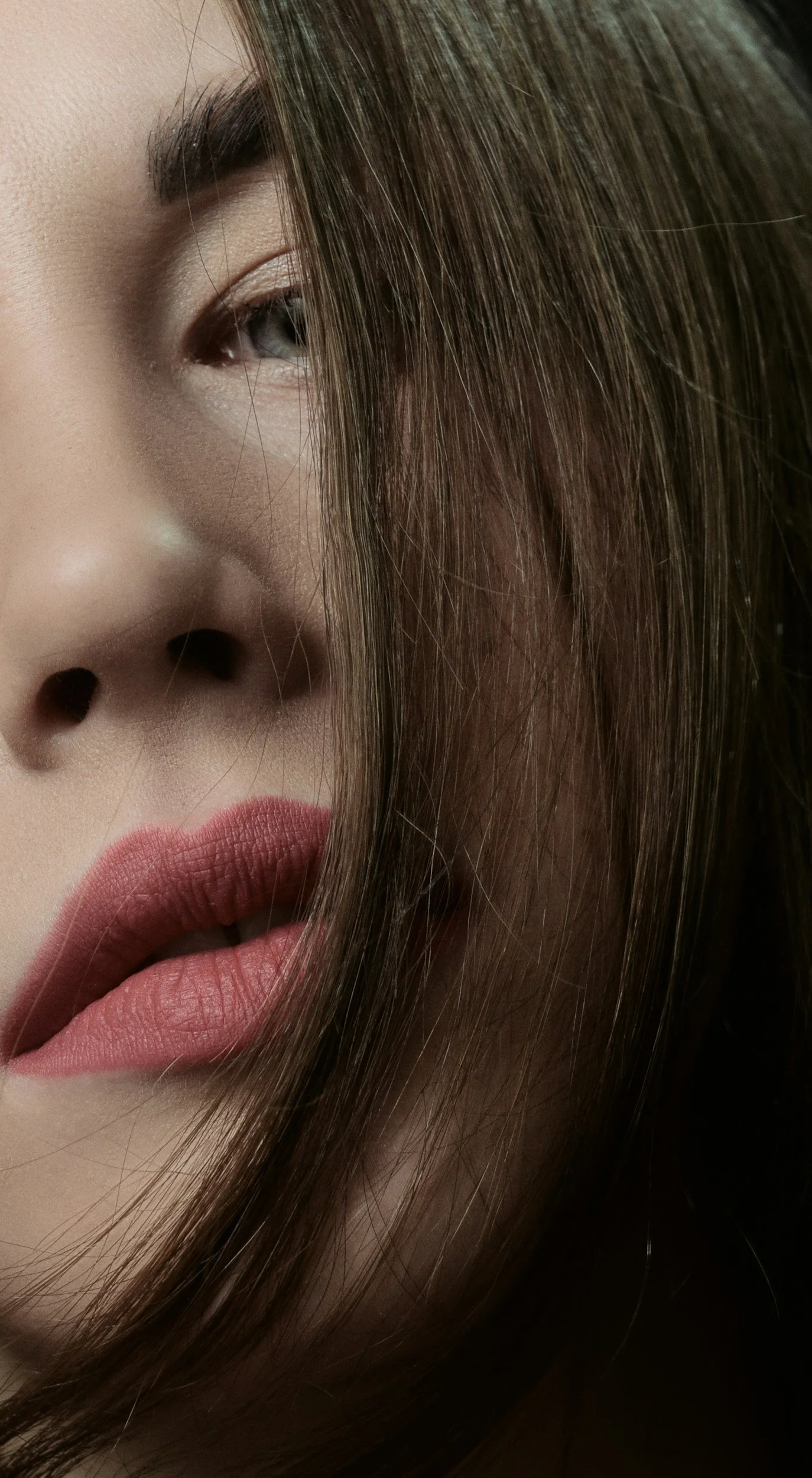 Close-up of a woman's face showing her eye, nose, lips, and brown hair covering part of her face.
