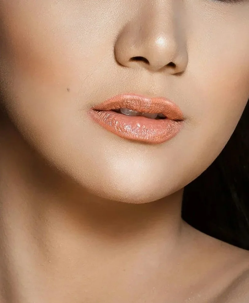 Close-up of a woman's face, showing lips with peach-colored lipstick and smooth skin.