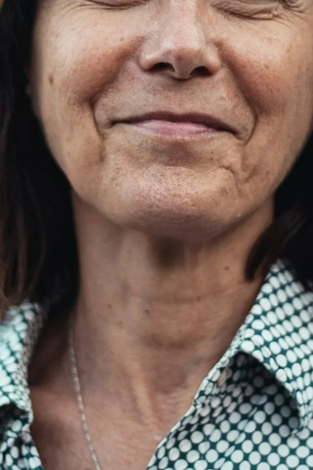Close-up of a smiling older woman with visible smile lines and a patterned shirt.