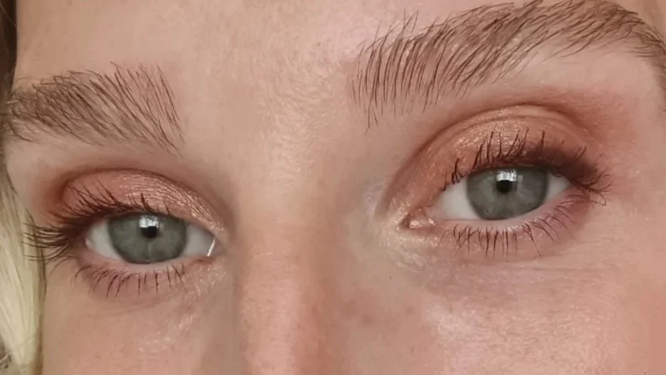 Close-up of a woman's eyes with light eye makeup, including eyeshadow and mascara, and light eyebrows.