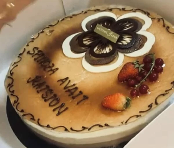 Gâteau rond à la crème, décoré de fleurs en chocolat, fraises, cerises, et écriture en chocolat
