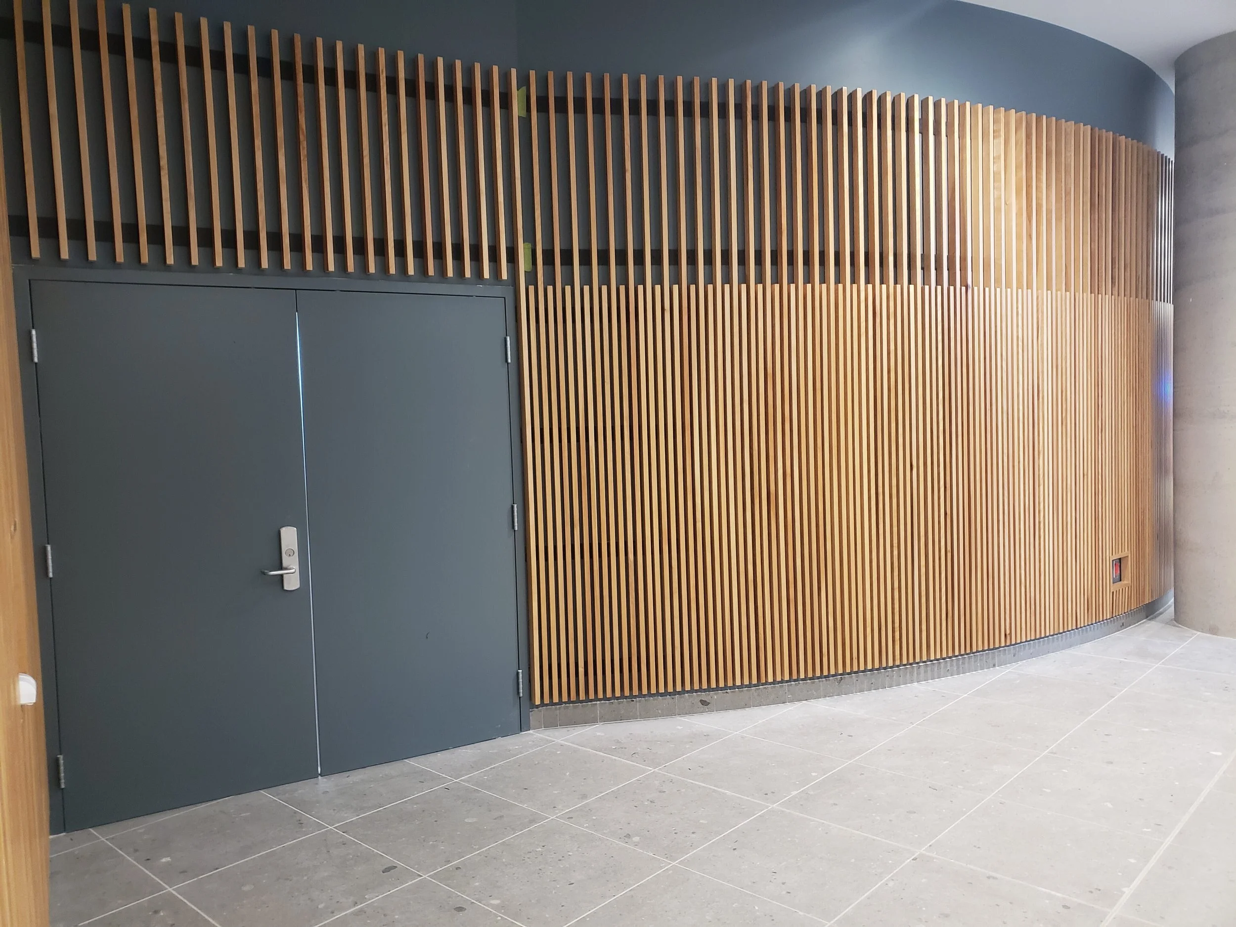 A modern interior wall with a wooden slat design, gray door, and gray tiled floor.