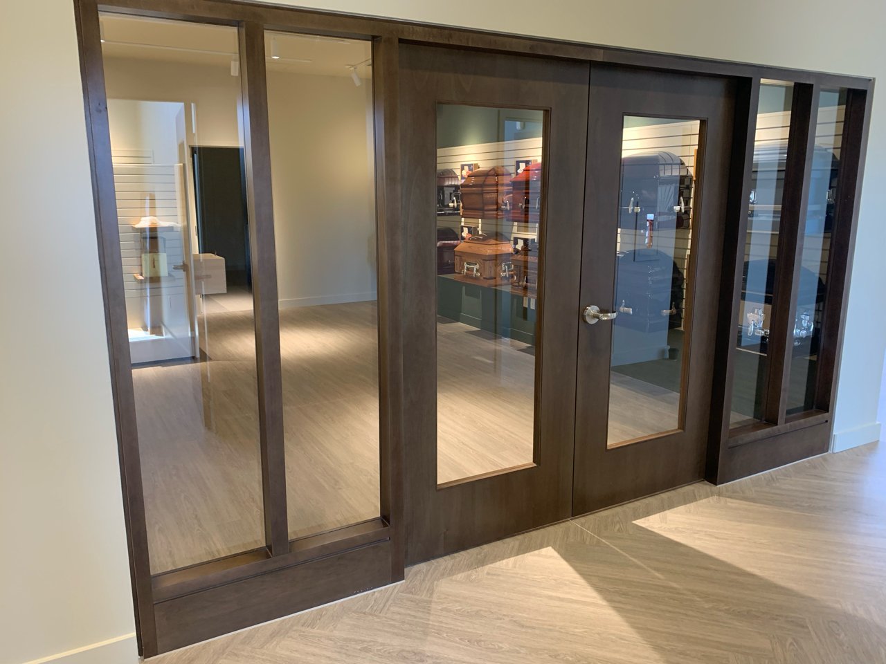 A wooden display cabinet with glass panels, standing on a light wood floor in a store or showroom.
