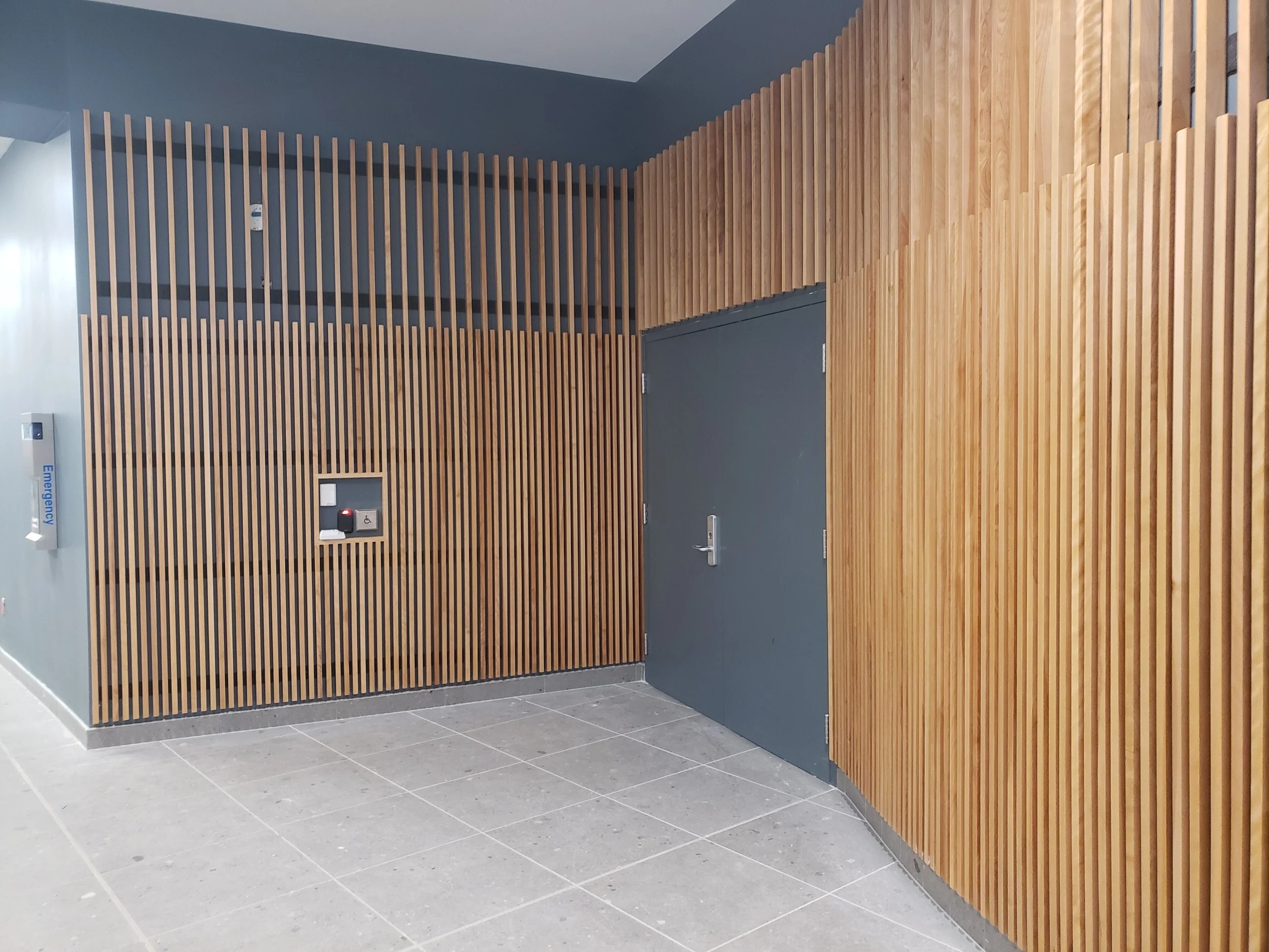 Interior with wood paneling and gray walls, including a closed gray door, an emergency oxygen mask, and an emergency call button.