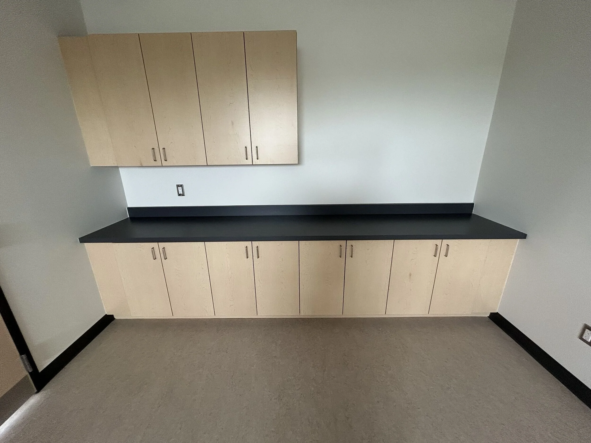 Empty room with beige cabinets, black countertop, gray walls, and black baseboards.