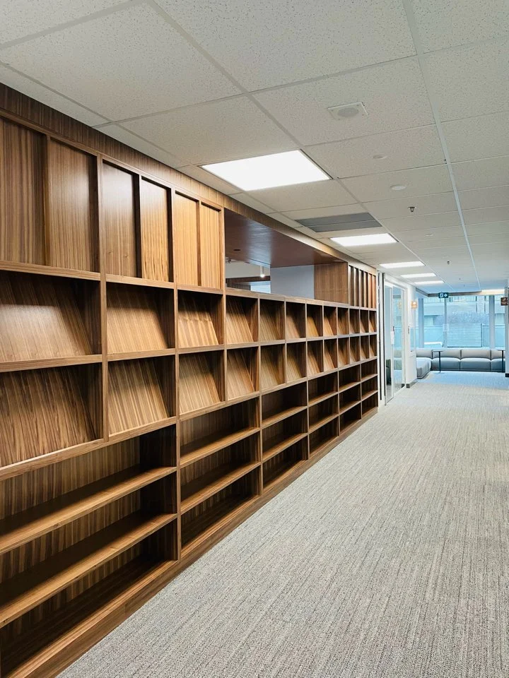 Empty wooden bookshelf in a modern office corridor with a view of a lounge area at the end of the hall.