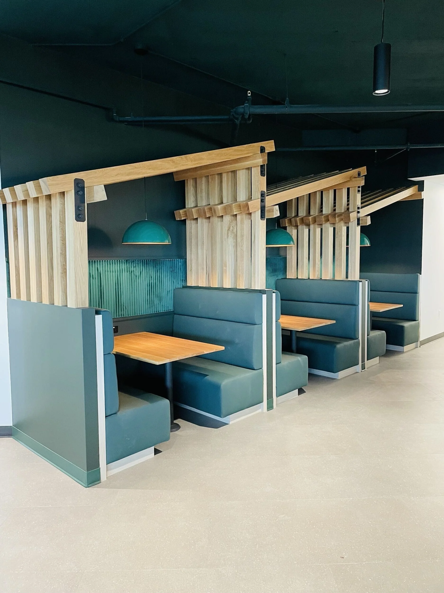 Modern seating area with teal booths, wooden dividers, and teal pendant lights in a restaurant or cafe.
