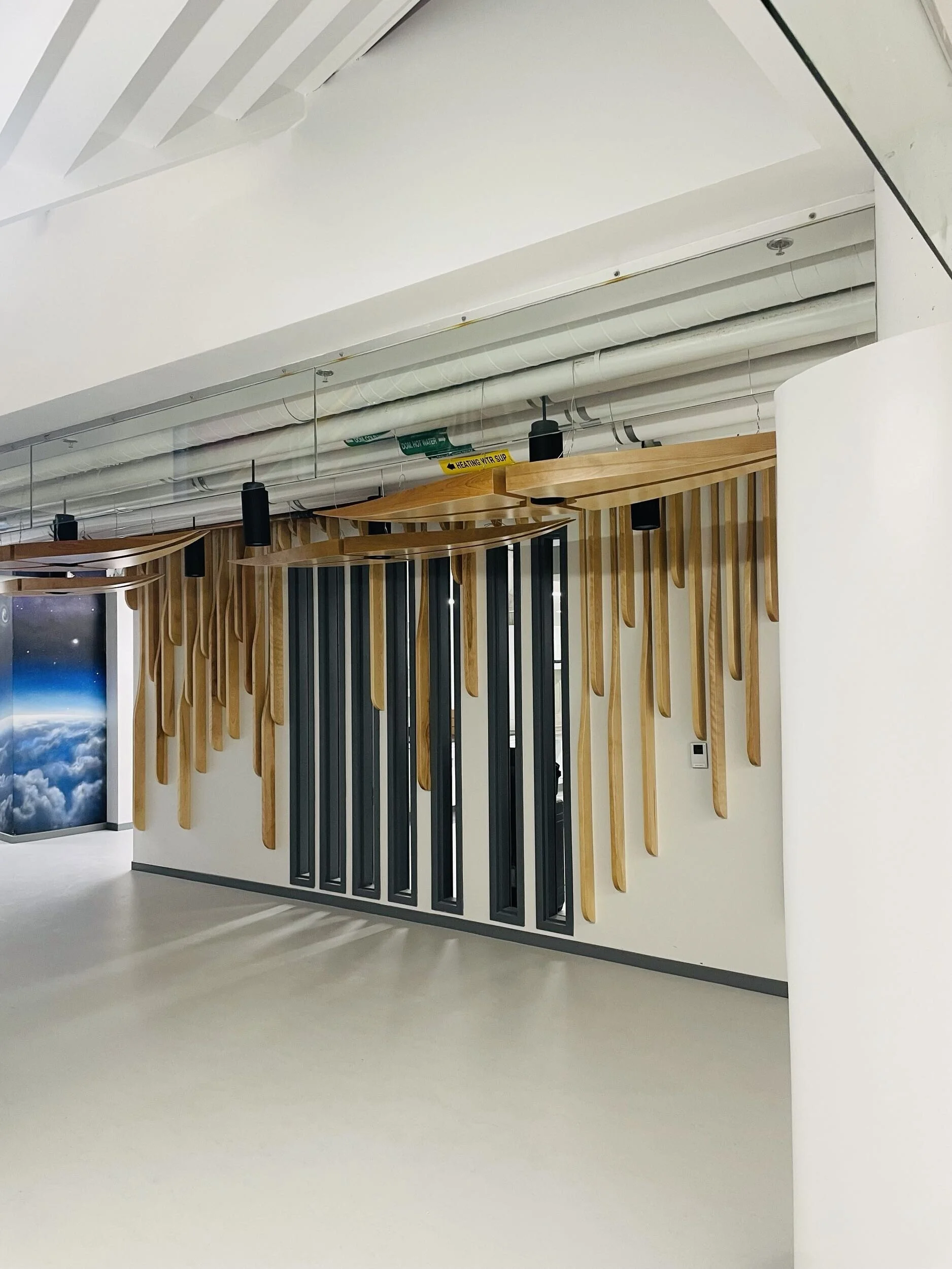 A modern interior space with a white ceiling, wooden decorative elements on a wall, black cylindrical pendant lights, and exposed white piping along the ceiling, with a blue and white Earth image on a vertical digital display on the wall.