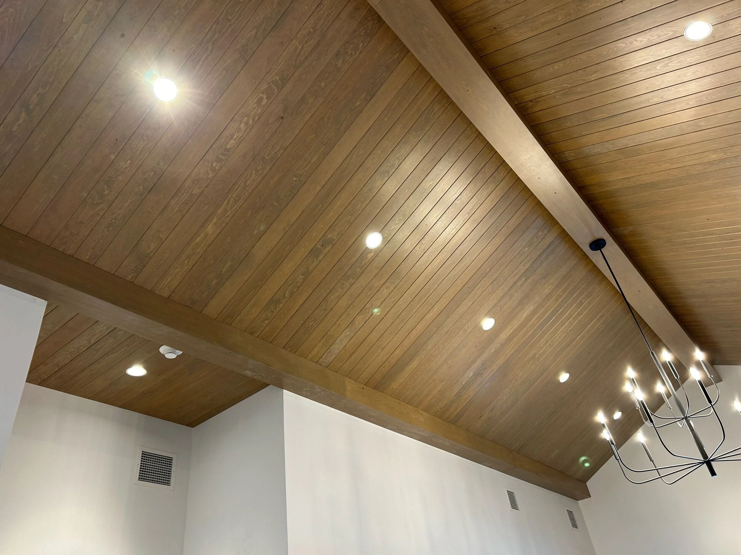 Wooden ceiling structure with several recessed lights and a modern black chandelier with multiple bulbs hanging from the ceiling.
