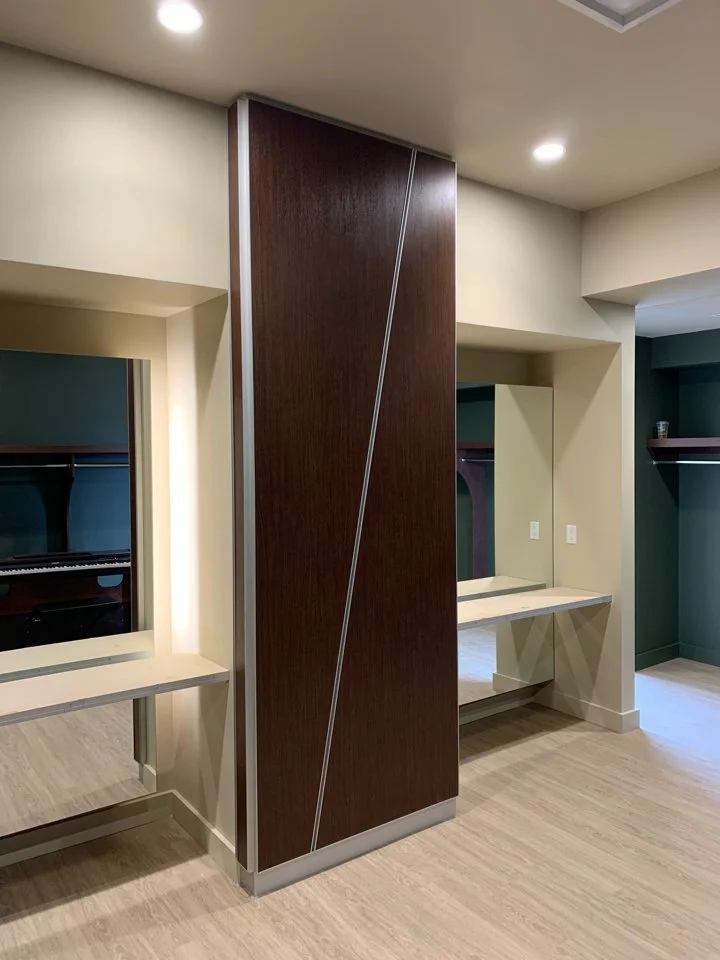 Interior view of a room with a partition wall, built-in desks with mirrors, and an open closet with shelves and a hanging rod.