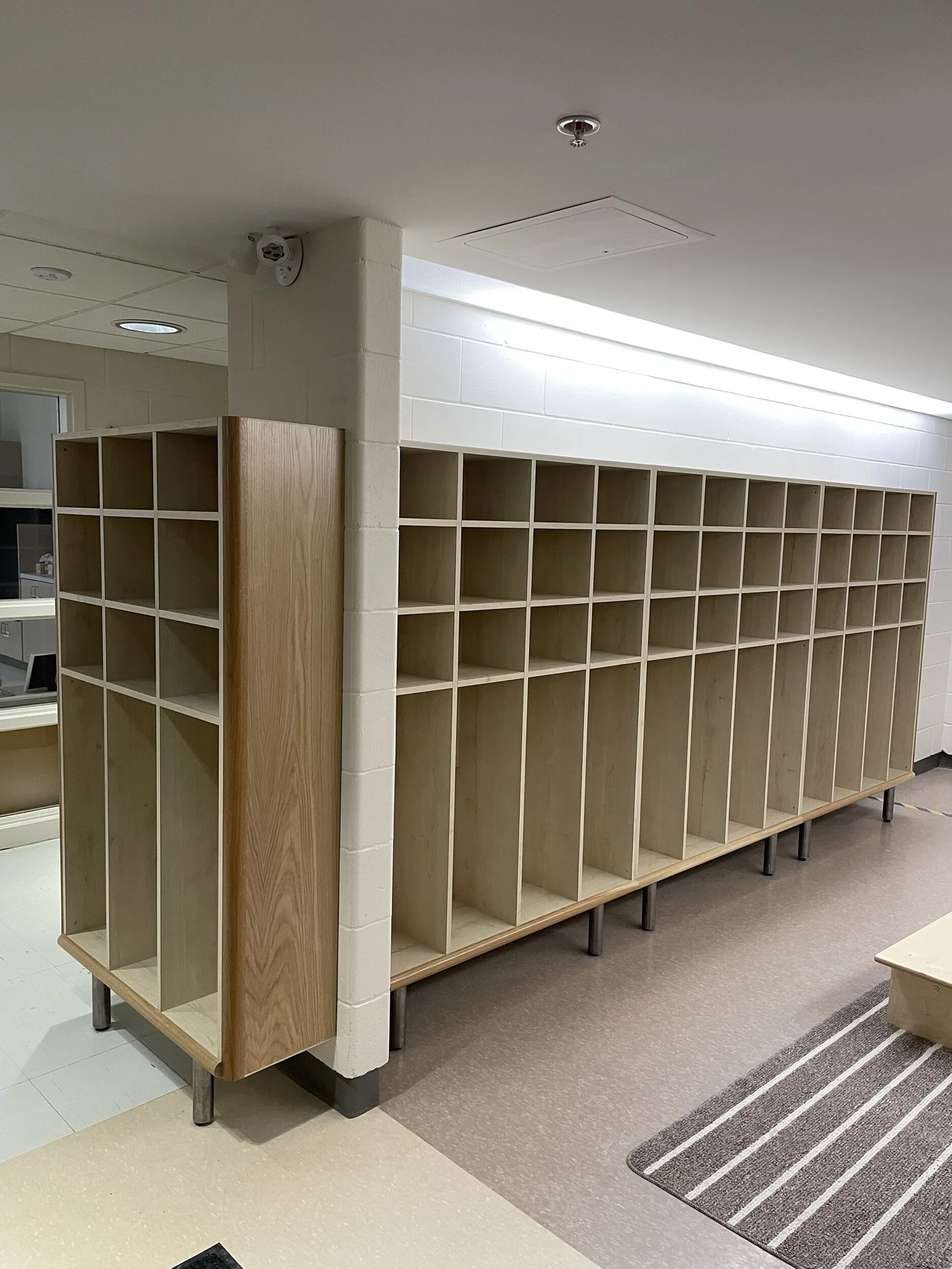 Empty wooden cubicles in a room with neutral-colored flooring and a striped rug.