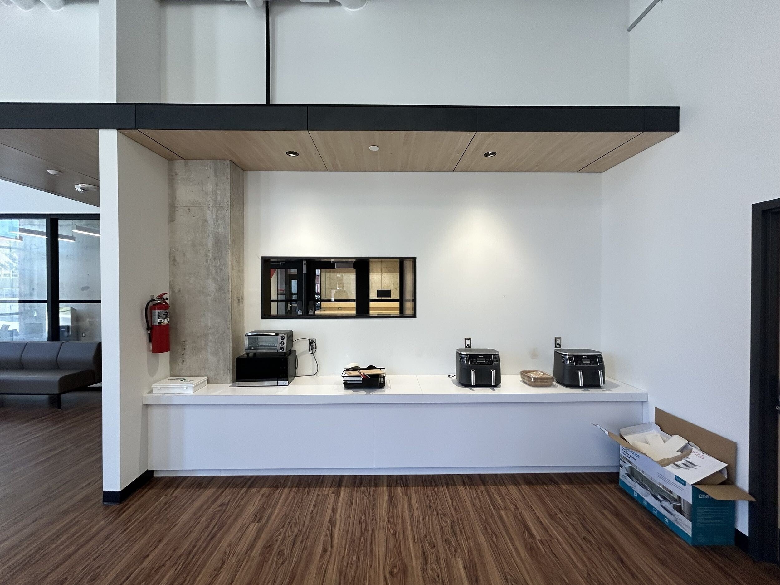 Interior of a modern office or reception area with a white counter, square black and wood accents, and various small appliances and boxes around.